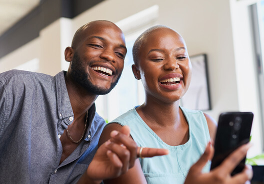 A man and women smile as they search for and review life and funeral insurance options via a phone.