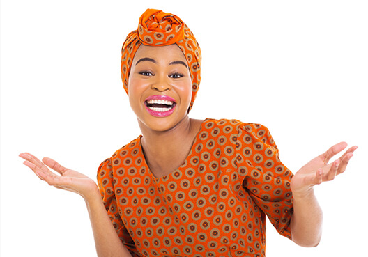 A woman wearing an orange patterned dress and headscarf smiles and gestures with her hands.